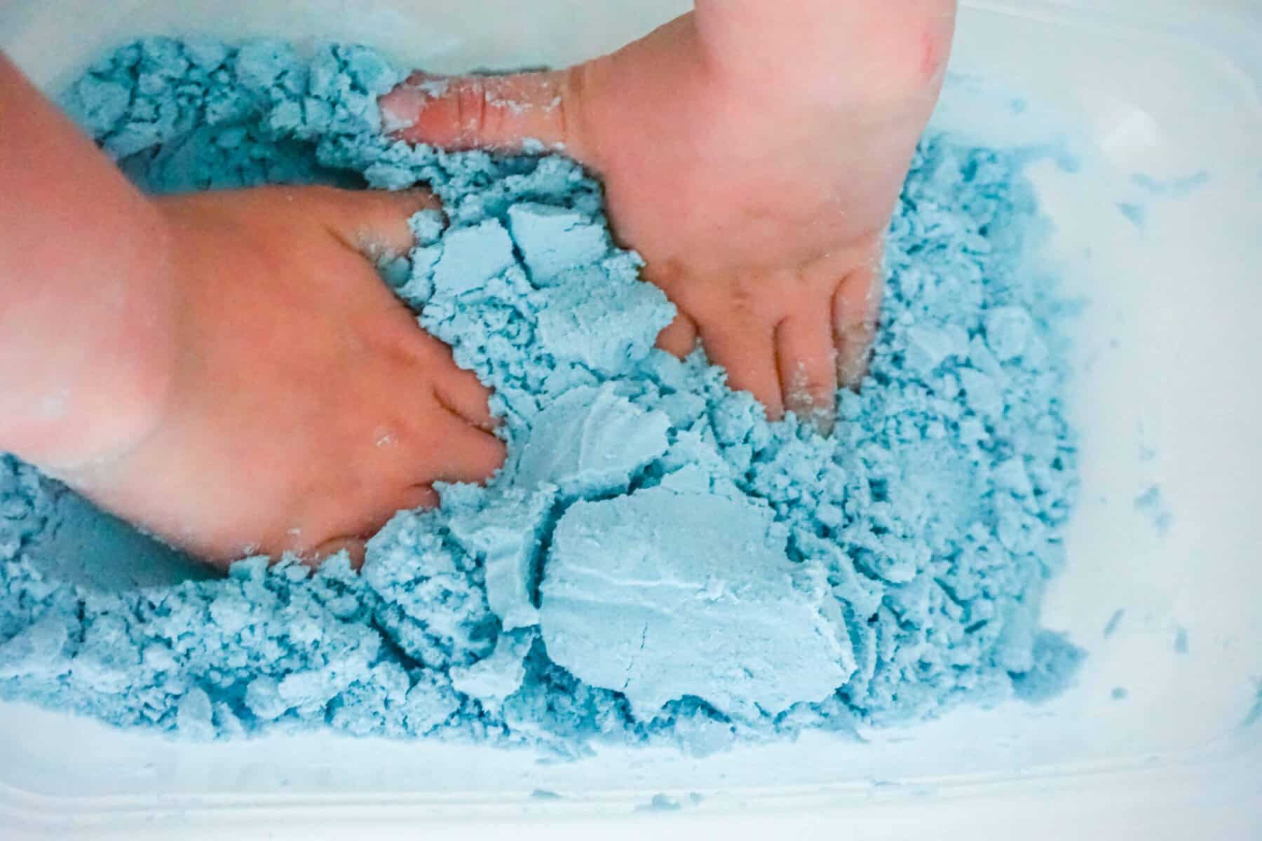 Child playing with blue kinetic sand for sensory activity.