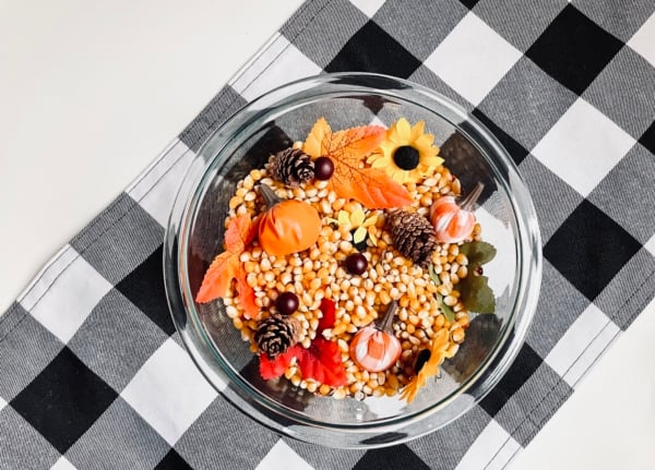 A bowl filled with corn, sunflowers, and pumpkins.