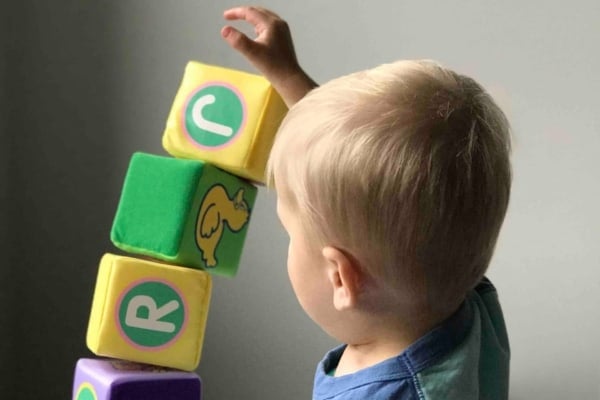 A toddler is engaged in early intervention services while playing with a stack of blocks.