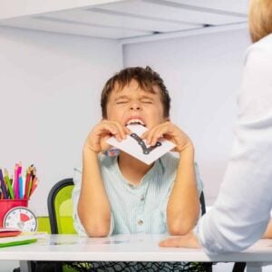A young boy is sitting at a desk with a woman, exhibiting behavior that aligns with his iep goals.