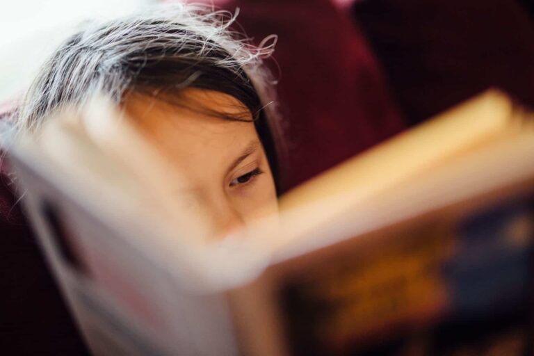 A young girl practicing her reading comprehension skills while enjoying a book on a comfortable couch.