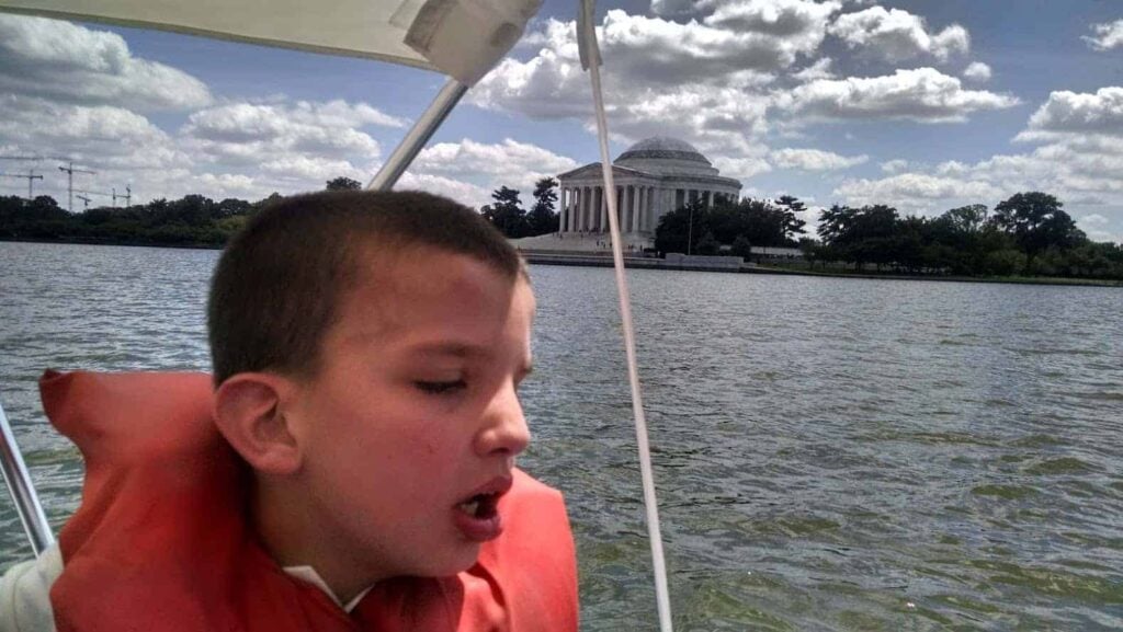 Paddle boat in water with child and life vest with monument in background