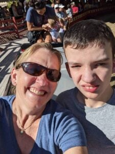 A woman with sunglasses and a blue top is smiling at the camera, taking a selfie with a young man in a blue top who looks into the camera with a transition iep goals bank half-smile