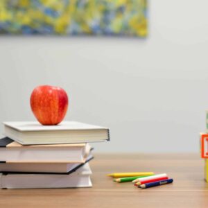 An apple sits on top of a stack of books, representing that it is crucial to set specific iep goals and refer to an iep goal bank for guidance.
