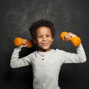 A child showcasing their strengths by lifting weights in front of a chalkboard.