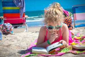Girl on beach reading a book from her summer reading program